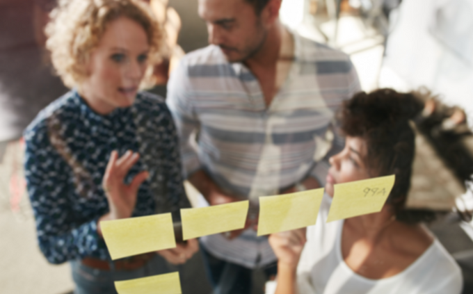 Two women and a man looking at post its during a team brainstorm meeting